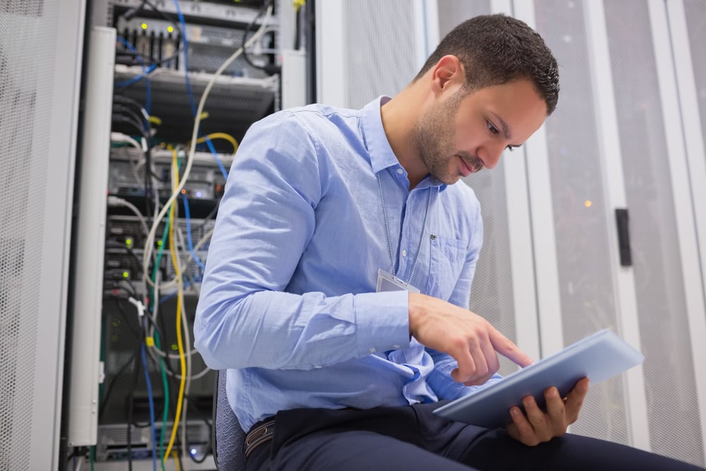 Man using tablet pc beside servers in data center